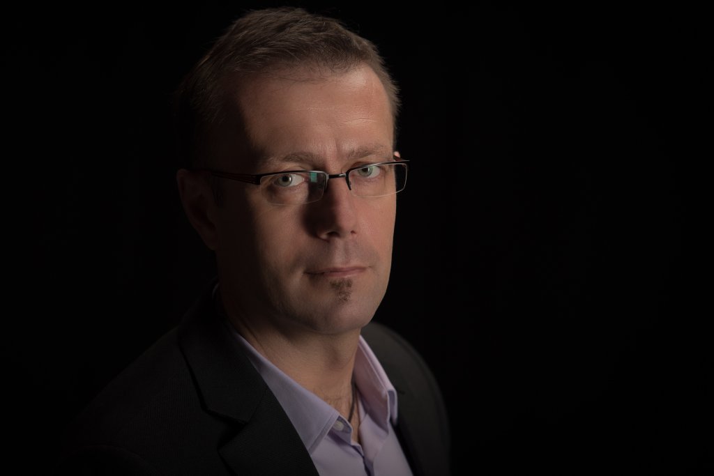 Szemüveges férfi sötét zakóban, fekete háttér előtt